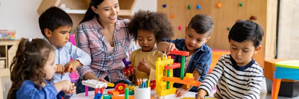 Happy Latin American teacher with a group of elementary students playing with toy blocks