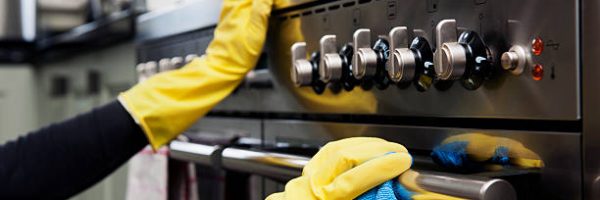 Closeup photograph of two hands cleaning the oven in a domestic kitchen.