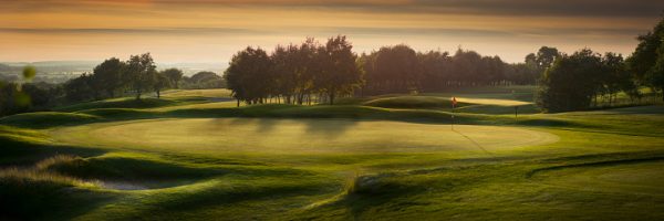 a panoramic scene of an empty golf course , with the shadows falling toward camera as the light fades .